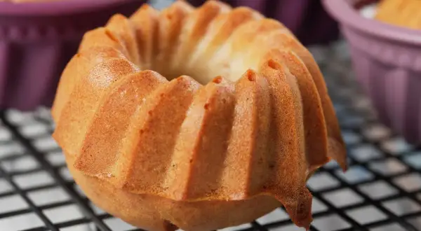 Złocista babka śmietankowa z charakterystycznymi żebrowaniami, wystudzana na kratce. W tle fioletowe foremki.