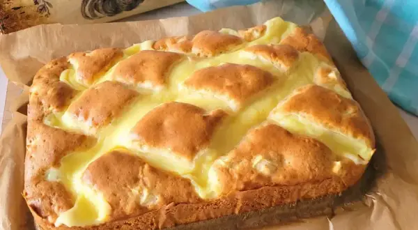 Wilgotne ciasto jogurtowe z budyniem, pieczone na papierze, z ozdobnym wałkiem w tle.