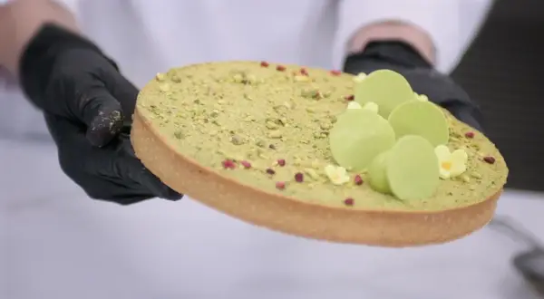 Ozdabianie mazurka pistacjowego z zielonymi czekoladowymi kuleczkami i malutkimi kwiatkami.