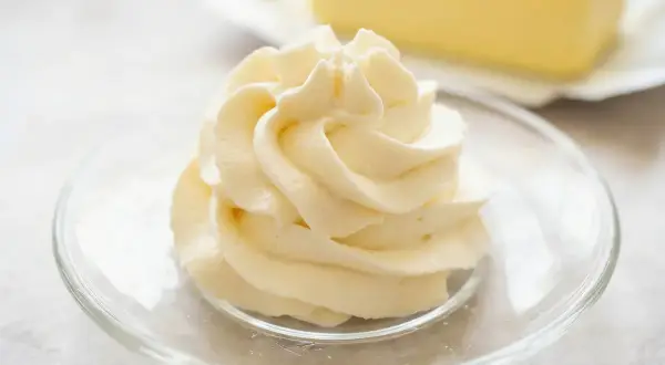 Krem patissiere w kształcie róży na talerzyku, w tle kostka masła.