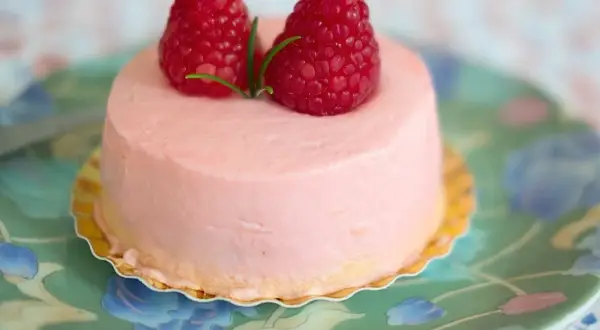 Delikatny krem malinowy z mascarpone do tortu, ozdobiony dwoma świeżymi malinami i listkiem.