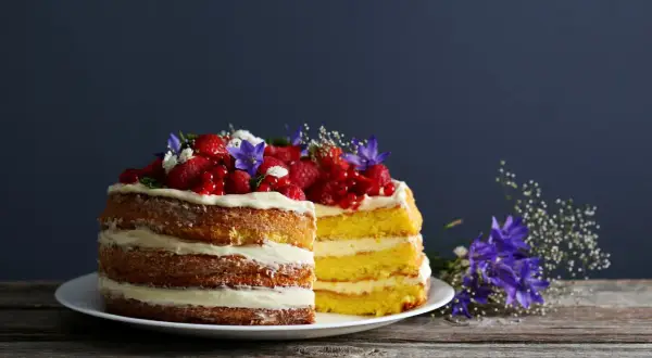 Dwa piętrowe naked cake z kremem i owocami leśnymi, ozdobione kwiatami.