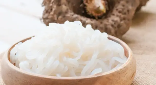 Miska pełna białego makaronu z mąki konjac, obok bulwa tej rośliny.