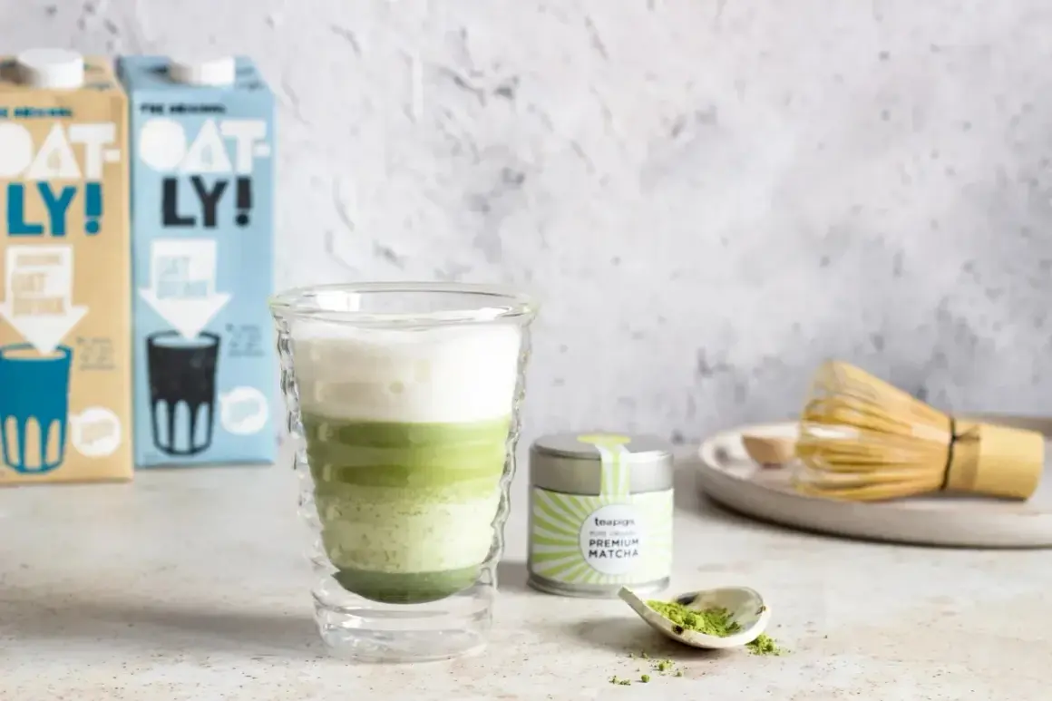 Warstwowy napój z zielonej herbaty matcha w szklance, obok puszka z napisem "PREMIUM MATCHA" i bambusowa miotełka.
