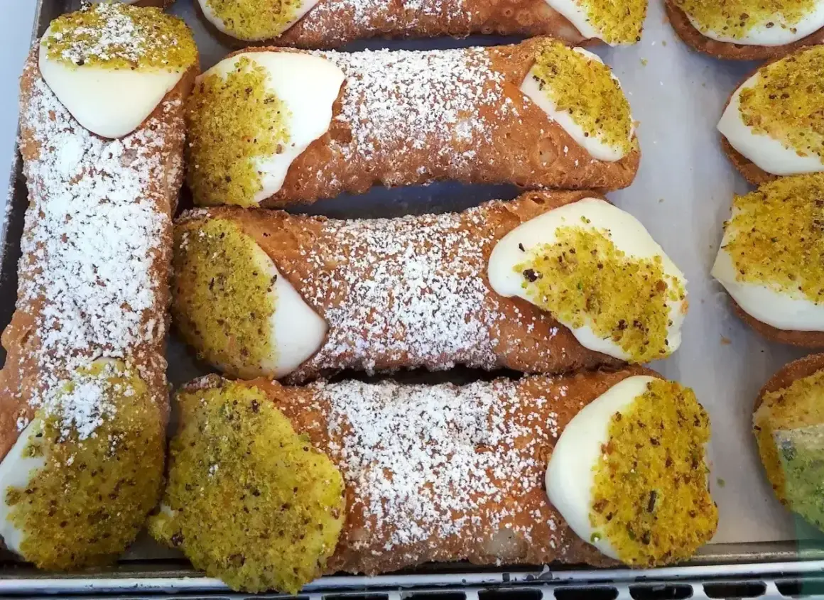 Chrupiące rurki wypełnione kremem, posypane cukrem pudrem i pistacjami. Pyszne **cannoli** czekają!