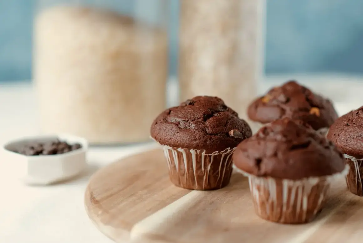 Puszyste muffinki czekoladowe, idealne na każdy przepis. W tle słoiki z cukrem i mąką.