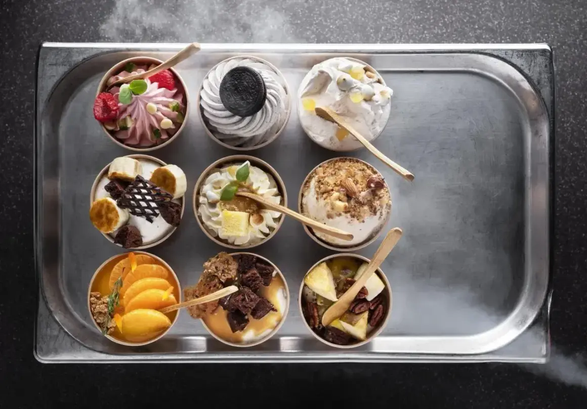 Dziewięć deserów typu parfait na tacy: malinowy, oreo, z orzechami, bananowy, pomarańczowy i inne.