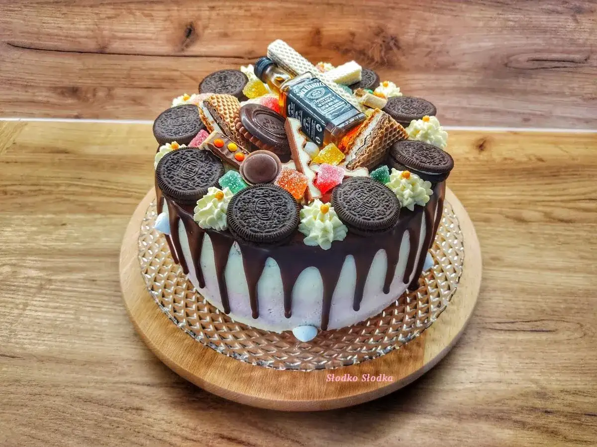 Tort ozdobiony ciasteczkami Oreo, waflowymi rurkami, żelkami i buteleczką Jack Daniel's. Prosta polewa czekoladowa z czekolady spływa po bokach.