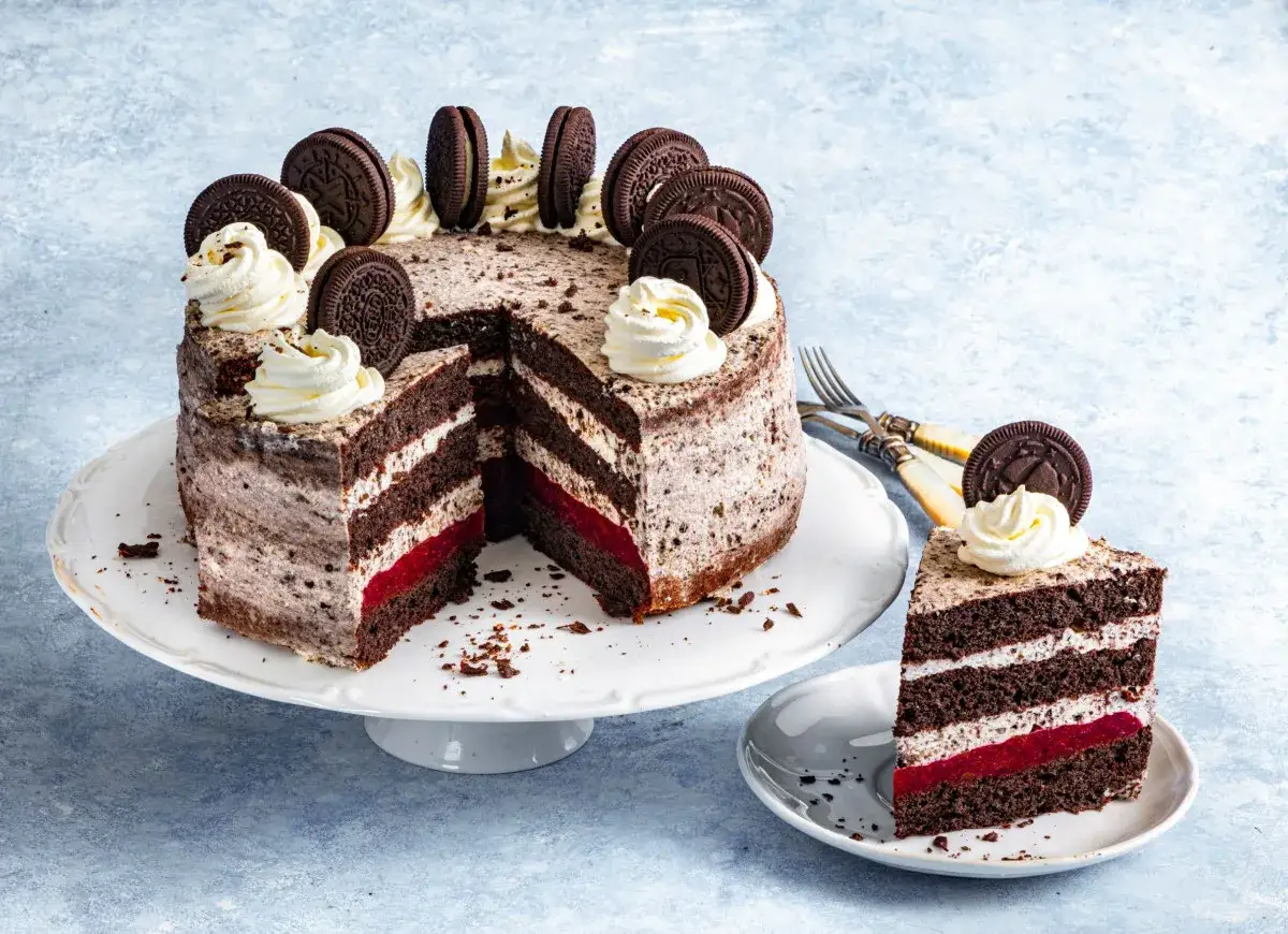 Pyszny tort z warstwami ciemnego ciasta, kremu i czerwonego dżemu. Całość ozdobiona bitą śmietaną i ciasteczkami Oreo. Idealna masa oreo do tortu.