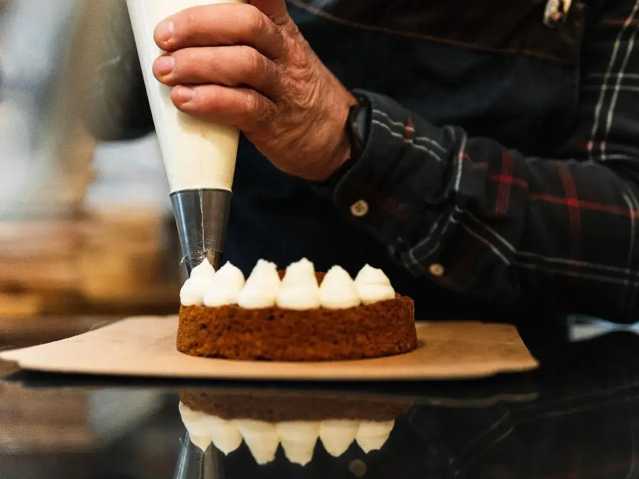 Ręka dekoruje ciasto kremem patissiere za pomocą rękawa cukierniczego.