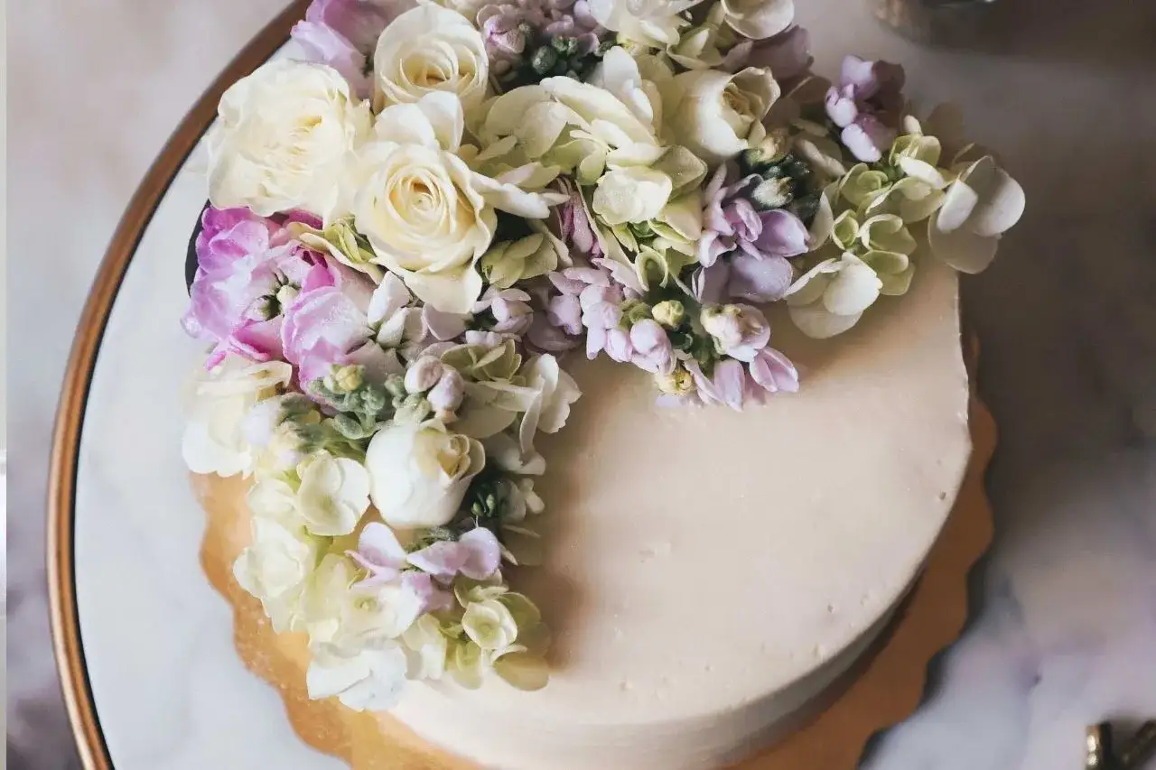 Elegancki naked cake ozdobiony bukietem białych i fioletowych kwiatów.