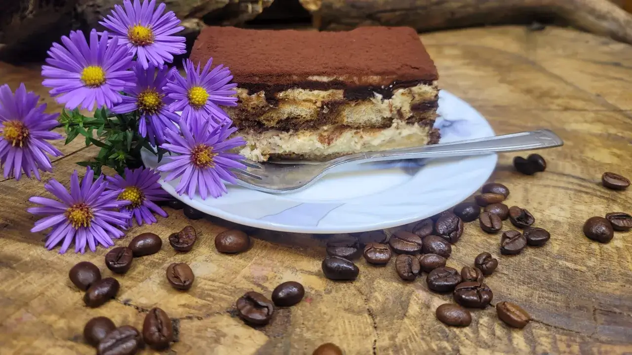 Pyszne tiramisu bez alkoholu, udekorowane fioletowymi kwiatami i ziarnami kawy, czeka na widelczyk.