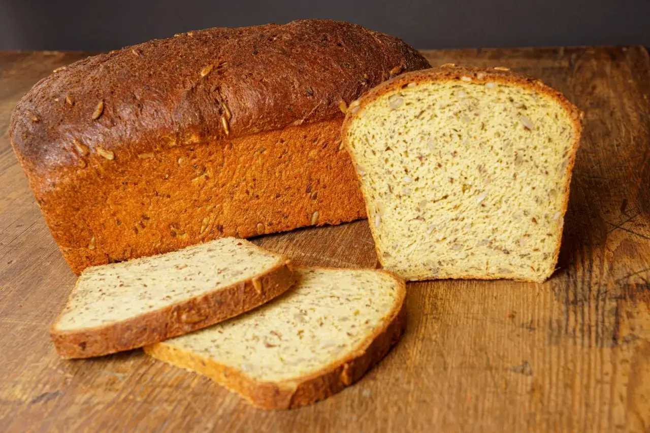 Chleb keto z ziarnami na drewnianej desce. Kromki i cały bochenek wyglądają apetycznie.