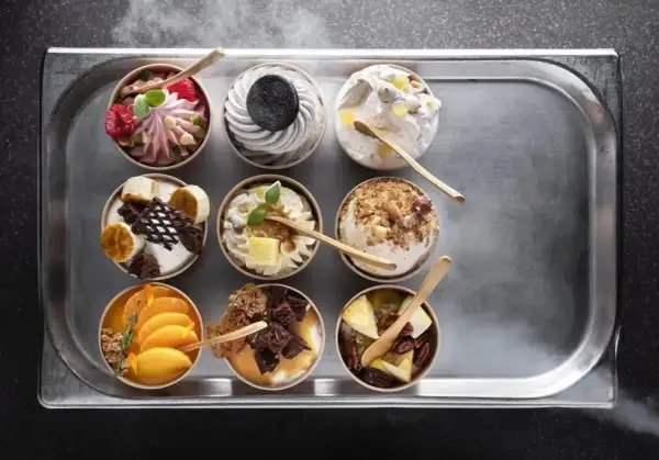 Dziewięć deserów typu parfait na tacy: malinowy, oreo, z orzechami, bananowy, pomarańczowy i inne.