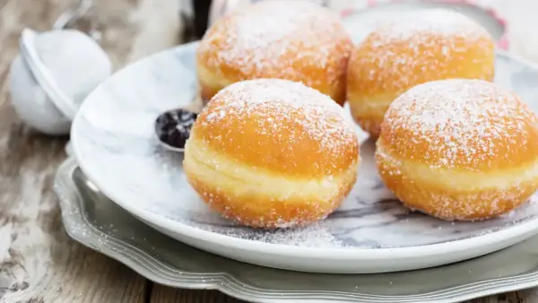 Pączki z ziemniakami Ewy Wachowicz, puszyste i obsypane cukrem pudrem, kuszą na talerzu.