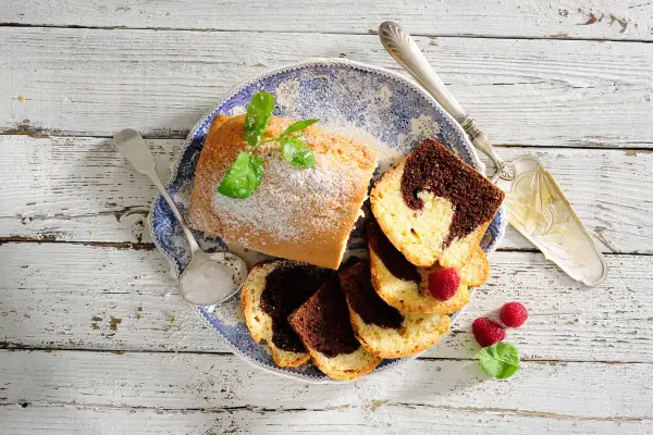 Babka piaskowa przepis babci: pyszne ciasto marmurkowe, posypane cukrem pudrem, z malinami i miętą na talerzu.