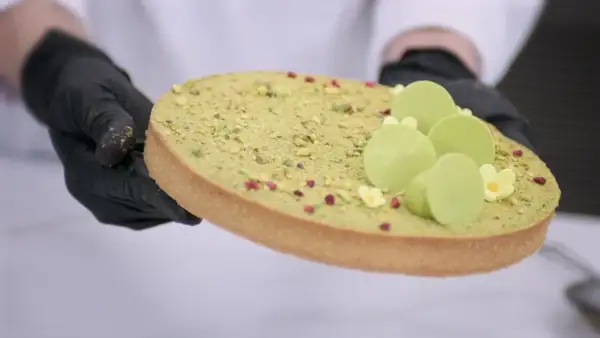 Ozdabianie mazurka pistacjowego z zielonymi czekoladowymi kuleczkami i malutkimi kwiatkami.