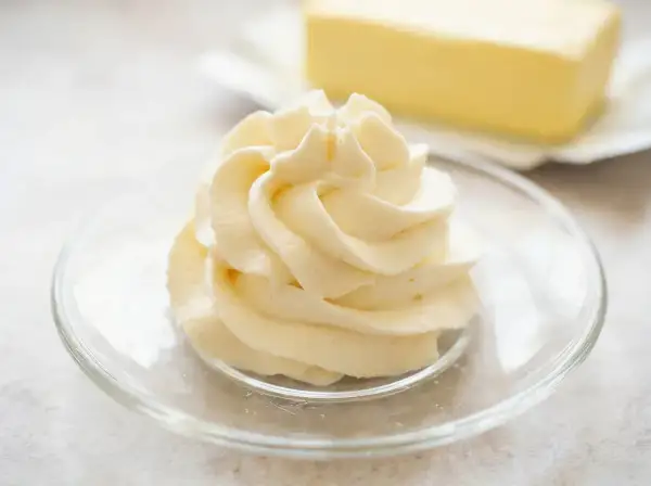 Krem patissiere w kształcie róży na talerzyku, w tle kostka masła.