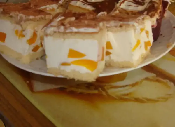 Sernik z bitą śmietaną siostry Anastazji, z kawałkami brzoskwini, posypany kakao. Pyszny deser na talerzu.