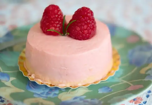 Delikatny krem malinowy z mascarpone do tortu, ozdobiony dwoma świeżymi malinami i listkiem.
