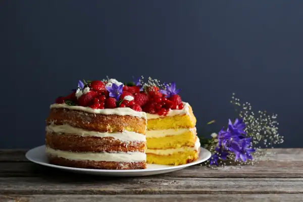 Dwa piętrowe naked cake z kremem i owocami leśnymi, ozdobione kwiatami.