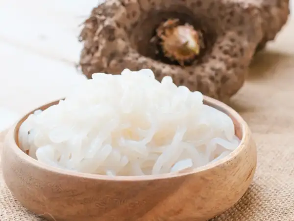 Miska pełna białego makaronu z mąki konjac, obok bulwa tej rośliny.