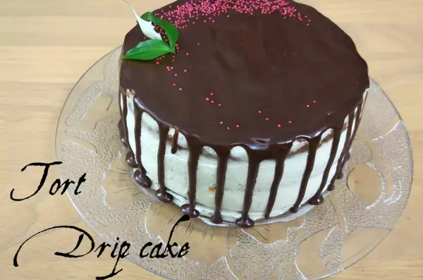 Pyszny tort drip cake z polewą czekoladową i różową posypką, ozdobiony listkami.